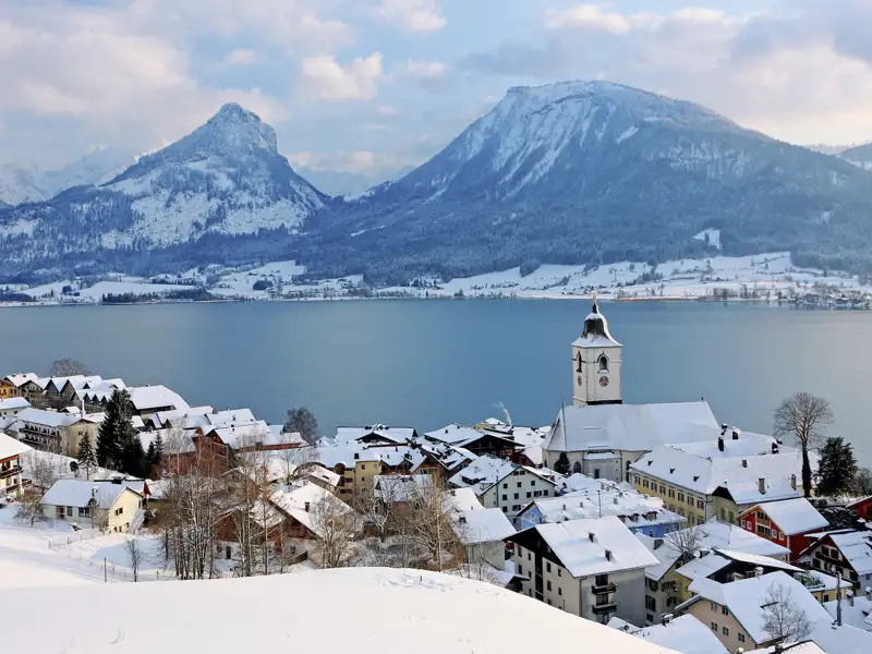 Winterliche Ansicht von St. Wolfgang am Wolfgangsee mit der Pfarrkirche und den verschneiten Bergen im Hintergrund.
