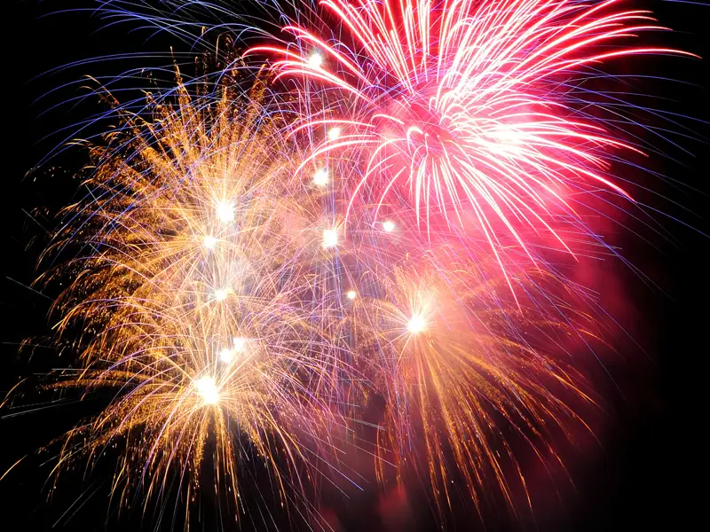 Leuchtend rotes und goldenes Silvester-Feuerwerk funkelt am Nachthimmel über dem Bodensee während der Eventreise in Lindau.