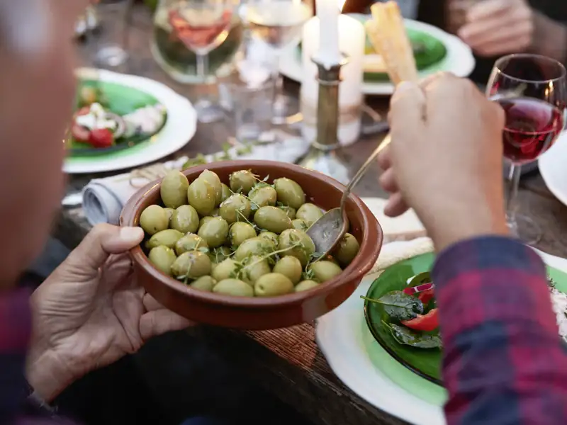 Hände nehmen mit einem Löffel grüne Oliven aus einer Tonschale bei einem gemeinsamen Abendessen auf einer Studiosus Genussreise in Istrien.