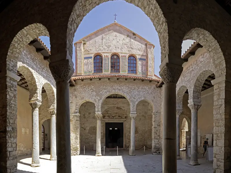 Blick durch die Arkaden des Atriums auf die historische Fassade der Euphrasius-Basilika in Poreč, ein UNESCO-Welterbe in Istrien. Ein wunderschöner Ausblick für unsere Studiosus Reisenden auf ihrer Eventreise.