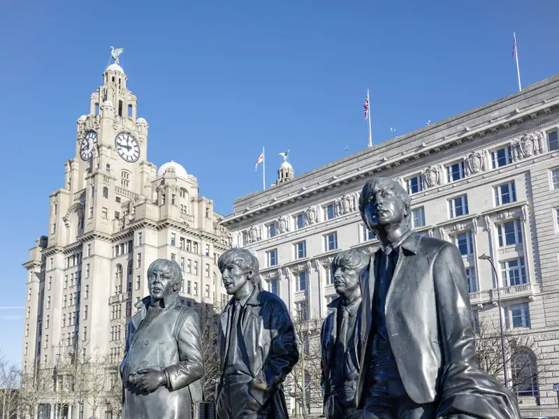 Die berühmte Bronzestatue der Beatles am Pier Head in Liverpool vor dem historischen Royal Liver Building bei Sonnenschein. Ein Highlight Ihrer Studiosus Gruppenreise.