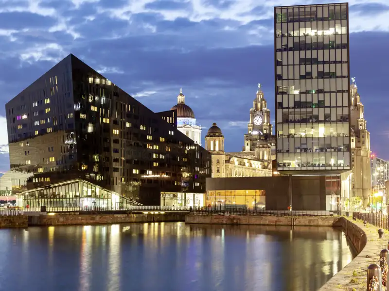 Abenddämmerung an der Waterfront in Liverpool mit den Three Graces und modernen Gebäuden, die sich im Wasser spiegeln.
