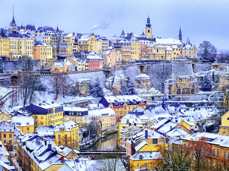 Winterlicher Blick auf die verschneite Altstadt von Luxemburg mit bunten Häusern und dem Fluss Alzette im Stadtteil Grund.