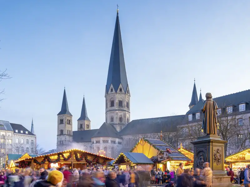 Festlich beleuchteter Weihnachtsmarkt auf dem Bonner Münsterplatz mit dem Beethoven-Denkmal und dem Münster bei Dämmerung. Ein Highlight Ihrer Studiosus Silvesterreise.