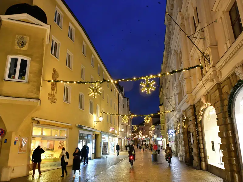 Eine Gasse in der Altstadt von Regensburg ist zur blauen Stunde festlich mit leuchtenden Schneeflocken geschmückt.