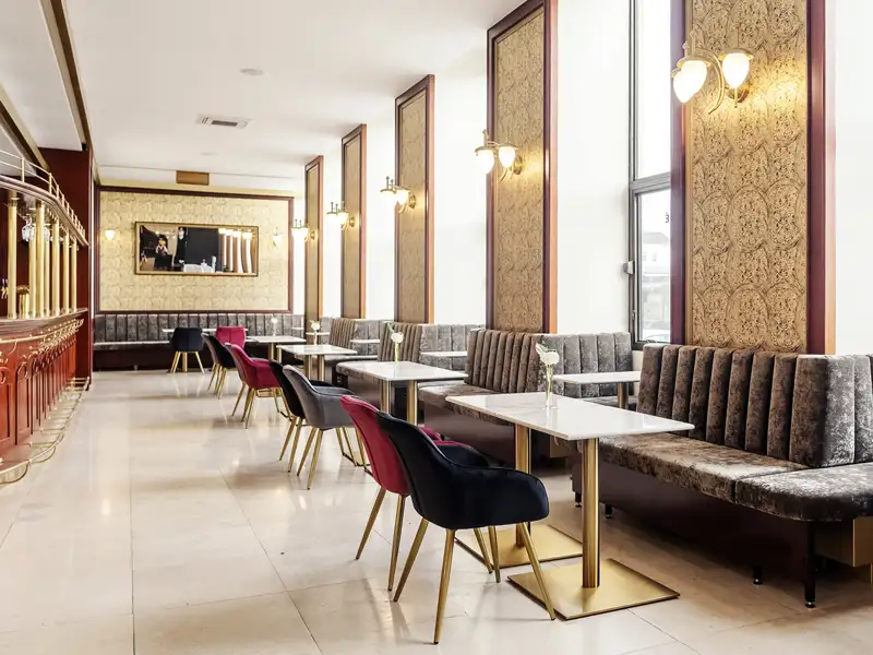 Elegantes Interieur der Hotelbar im Grandhotel Brno mit gepolsterten Samtbänken, Stühlen und kleinen Tischen bei Tageslicht.