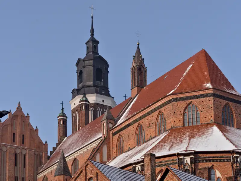 Die Marienkirche in Stargard, ein Meisterwerk der Backsteingotik, mit schneebedeckten Dächern vor klarem Winterhimmel.