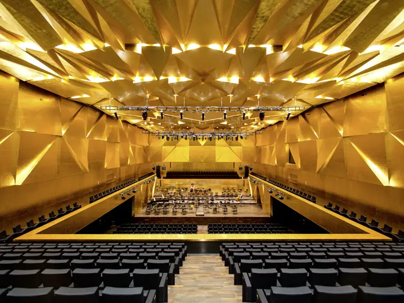 Der leere, goldene Konzertsaal der Stettiner Philharmonie mit seiner beeindruckenden, geometrischen Decken- und Wandgestaltung.
