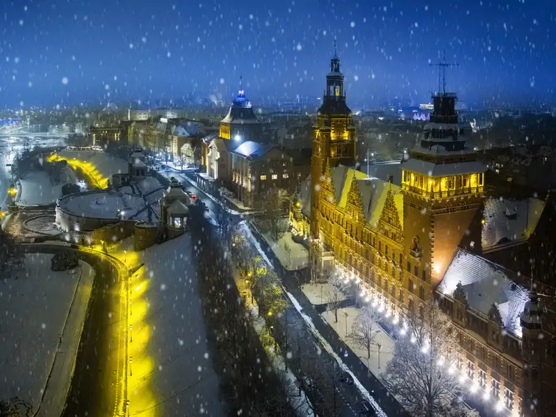 Die monumentale Hakenterrasse in Stettin bei Nacht, deren historische Gebäude im winterlichen Schneefall hell erleuchtet sind.