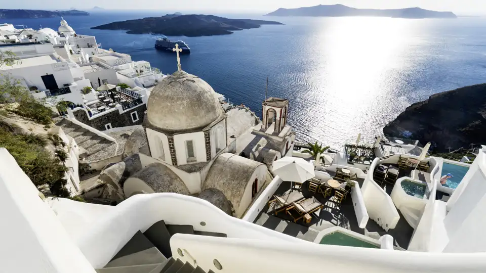 Weiße Gebäude und eine Kuppelkirche auf Santorin mit Blick auf das Meer und ein Kreuzfahrtschiff