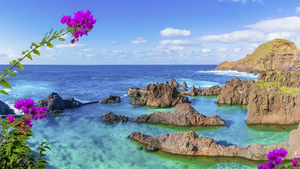 Die natürlichen Meeresschwimmbecken von Porto Moniz auf Madeira, ein im Reiseverlauf geplanter Besuch, mit türkisfarbenem Wasser und dunklen Lavafelsen unter blauem Himmel.