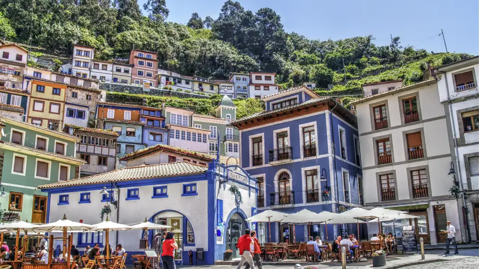 Sonnige Plaza im Fischerdorf Cudillero in Asturien mit bunten Häusern am Hang und belebten Terrassen von Cafés, ein Hingucker auf unserer Kulturreise mit Studiosus.