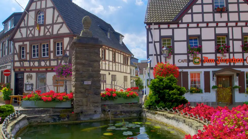 Blumengeschmückter Brunnen im historischen Zentrum von Rhöndorf mit Blick auf traditionelle Fachwerkhäuser sehen wir auf unserer Gruppenreise mit Studiosus.