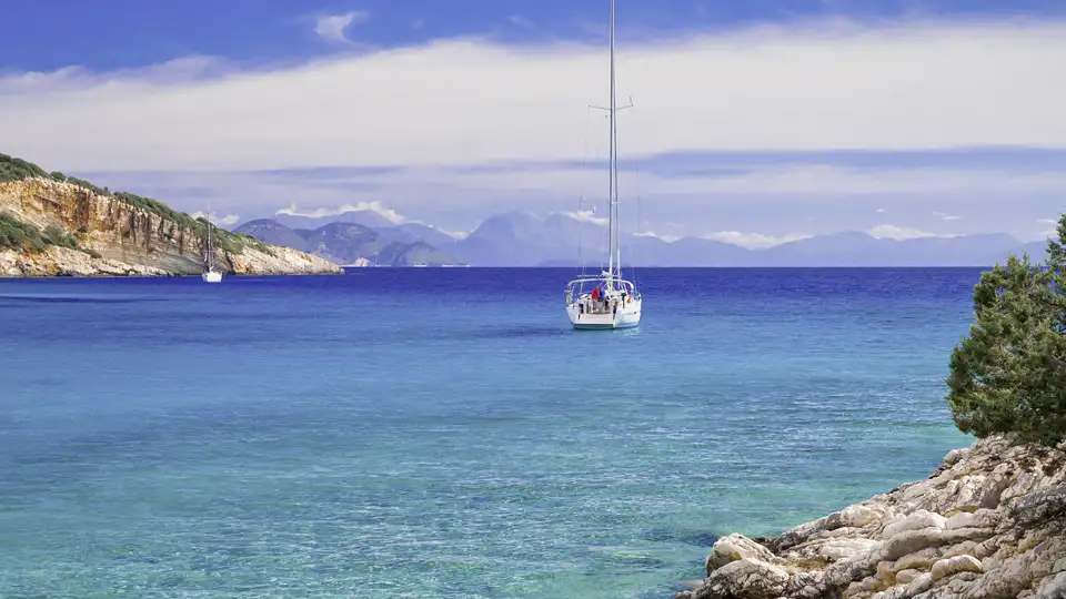 Ein Segelboot ankert in einer idyllischen Bucht vor Ithaka im türkisblauen Ionischen Meer, umgeben von Felsklippen. Ein schönes Fotomotiv auf unserer Studiosus Eventreise.