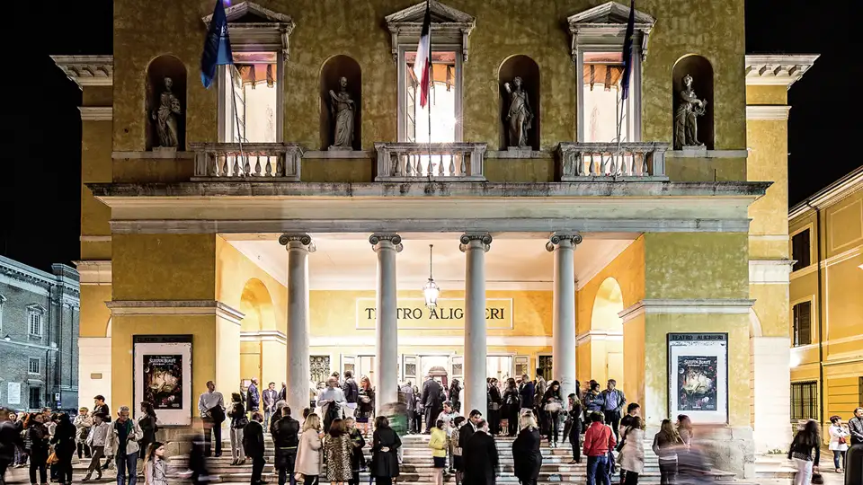 Elegant gekleidete Gäste einer Eventreise versammeln sich vor dem beleuchteten Teatro Alighieri in Ravenna.