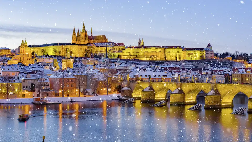 Die verschneite Karlsbrücke und die Prager Burg über der Moldau im abendlichen Lichterglanz bei Schneefall, sehen Sie auf Ihrer Eventreise mit Studiosus.