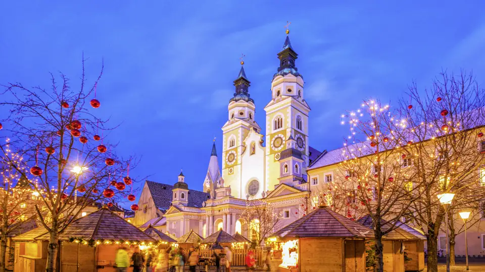 Stimmungsvoller Weihnachtsmarkt in Brixen mit beleuchteten Holzhütten vor der Kulisse des Doms in der Abenddämmerung, zu erleben auf ihrer Studiosus Silvesterreise.
