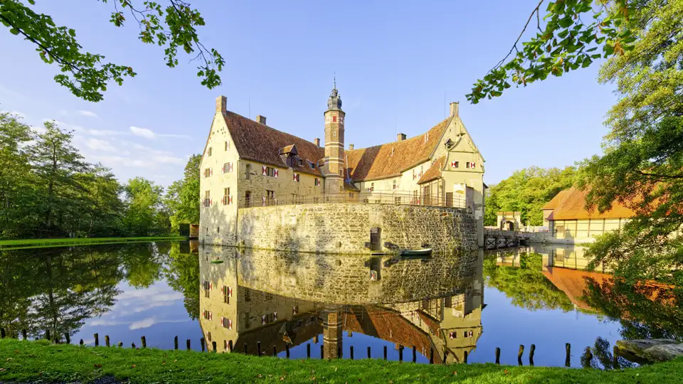 Die wehrhafte Burg Vischering im Münsterland spiegelt sich an einem sonnigen Tag im ruhigen Wasser des Burggrabens, auch sie auf ihrer Studiosus Studienreise werden diese wunderschön gelegene Burg auf ihrer Reise besichtigen dürfen.
