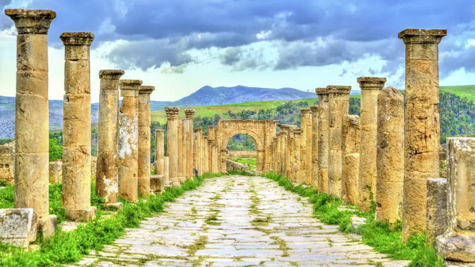 Gepflasterte Säulenstraße in der antiken Römerstadt Djemila, UNESCO-Welterbe in Algerien, mit grünen Bergen im Hintergrund, Auf ihrer Studiosus Eventreise zu besichtigen.