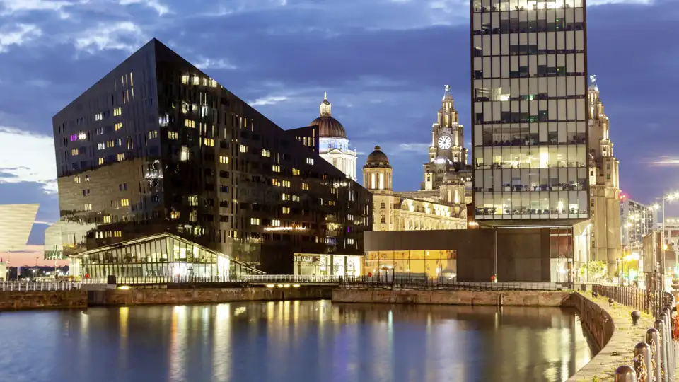 Abenddämmerung an der Waterfront in Liverpool mit den Three Graces und modernen Gebäuden, die sich im Wasser spiegeln.