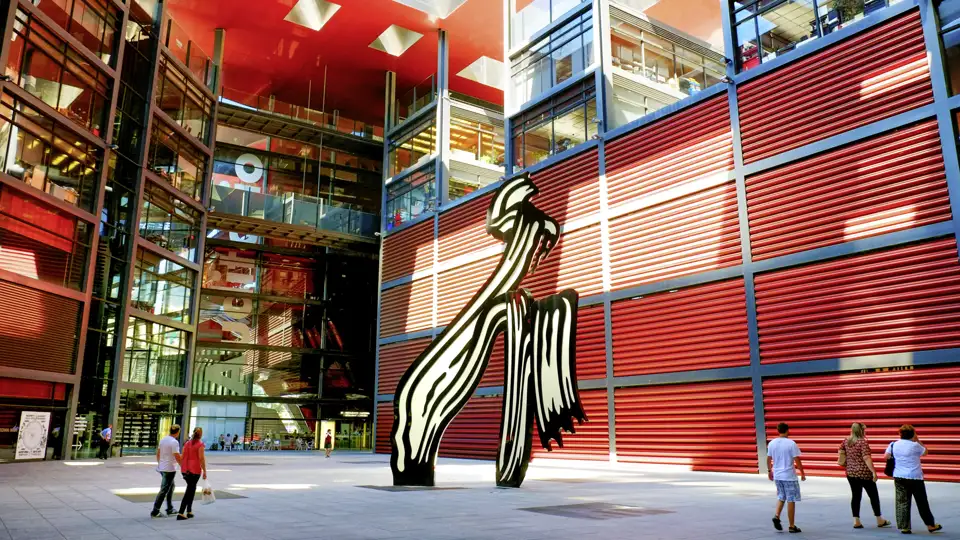 Studienreise in Madrid: Besucher im Innenhof des Reina Sofía Museums mit Roy Lichtensteins Skulptur und roter Fassade.