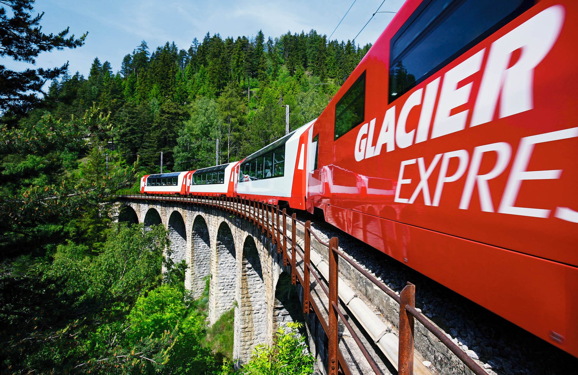 Der rot-weiß lackierte Zug Glacier Express fährt über eine Bahnbrücke.