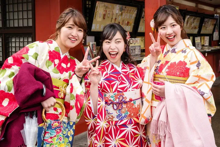 Drei junge Frauen in bunten Kimonos lächeln und posieren freundlich.