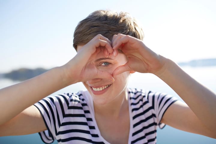 Eine junge Frau macht ein Herzzeichen vor der Kamera.