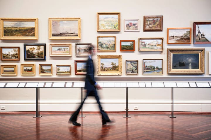 Ein Besucher geht durch eine Kunstgalerie mit Gemälden an der Wand.