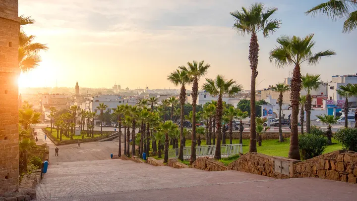 Ein Blick auf die marokkanische Stadt Rabat mit breiten Gehwegen und Palmbäumen im Vordergrund.